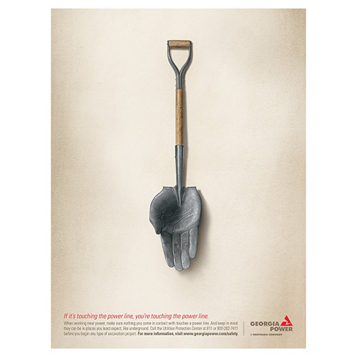 A shovel designed with a hand at its scoop emphasizes safety around power lines. Accompanying text warns of electric hazards during excavation.