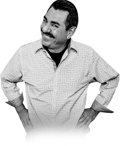 Smiling man with a mustache, wearing a patterned shirt, stands confidently with hands on hips. The image conveys a friendly, approachable demeanor.