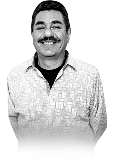 Smiling man with a mustache wearing a patterned shirt, against a solid green background. He exudes a friendly demeanor, suitable for a profile or introduction.