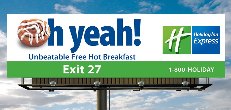 Billboard advertising Holiday Inn Express, featuring a cinnamon roll and the text “Unbeatable Free Hot Breakfast” with the direction to Exit 27.